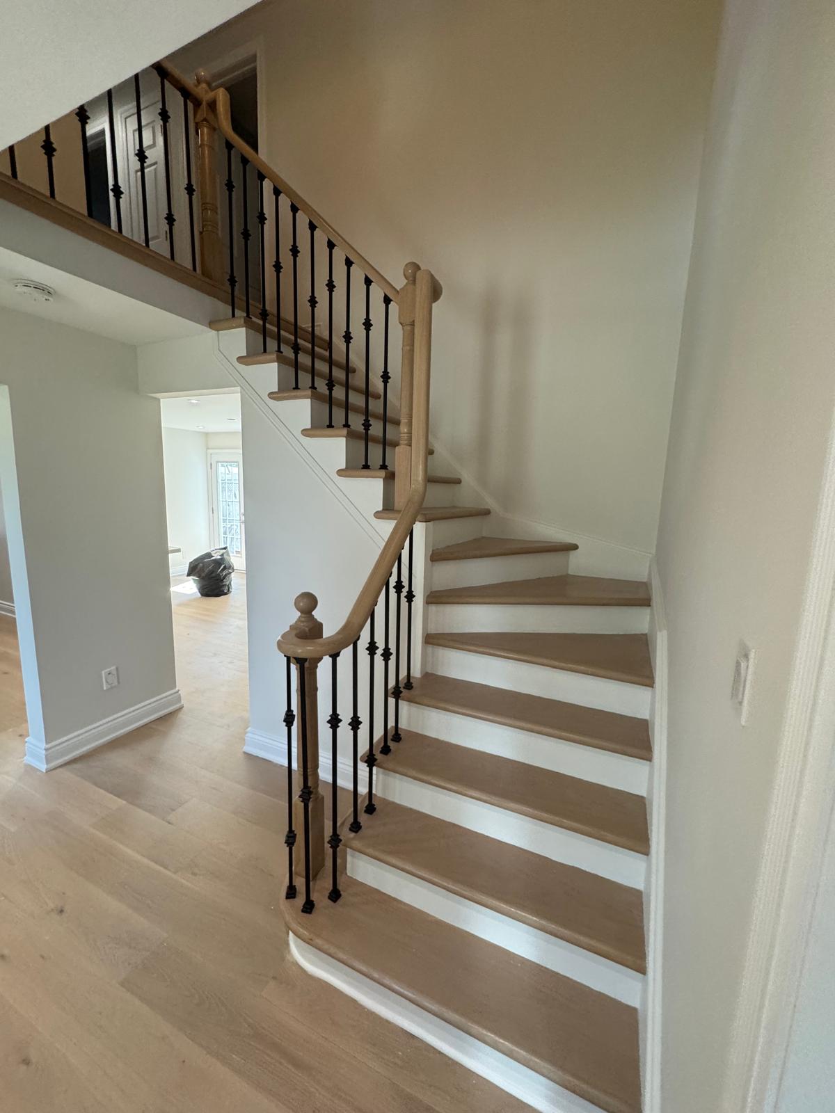 Wood staircase with black metal balusters and matching light wood flooring